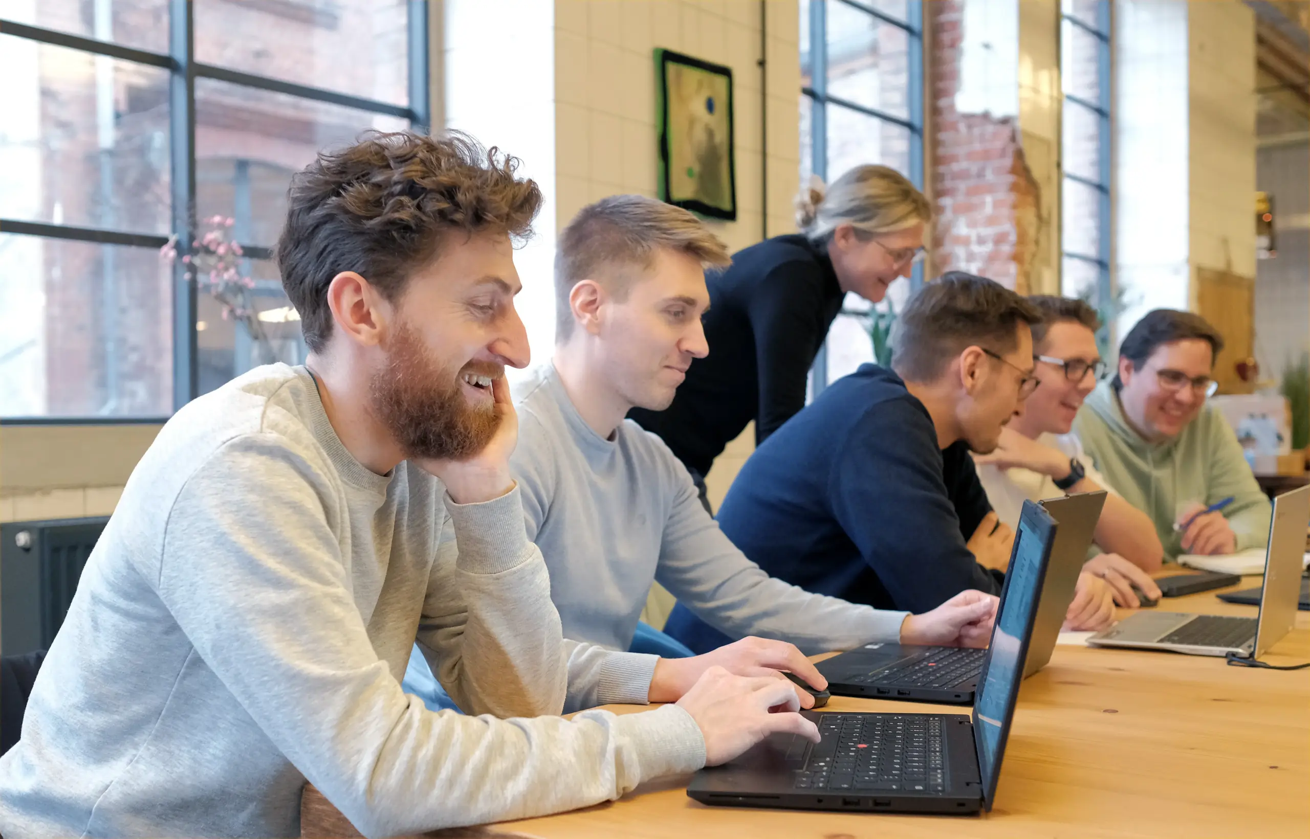 Ein Team von Mitarbeitern sitzt zusammen und arbeitet fokussiert an einem Laptop, symbolisiert Zusammenarbeit und Innovation.