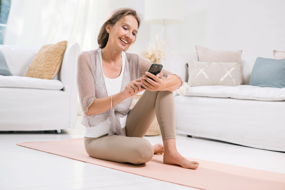 Frau sitzt mit Smartphine auf Yogamatte